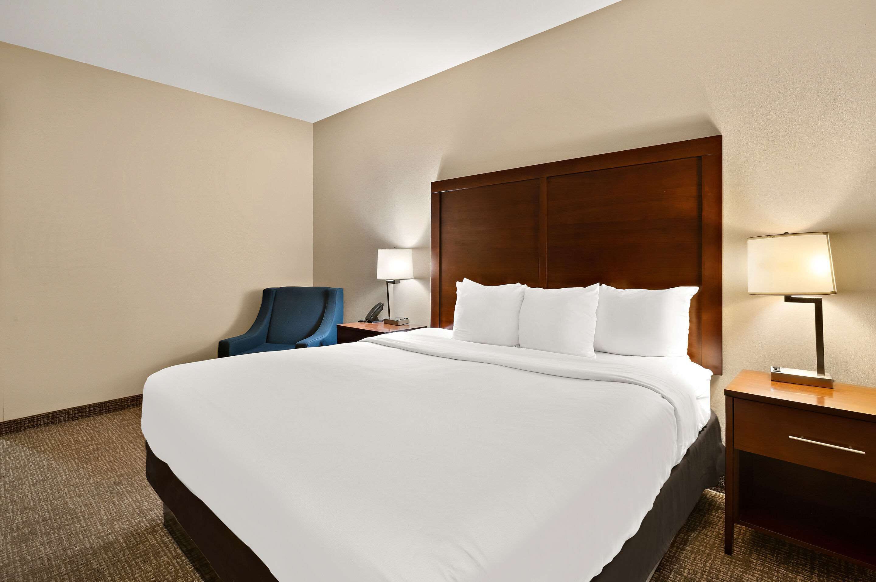 A hotel room with a large bed, a desk with a lamp, a chair, and a nightstand.