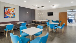 A modern dining area with blue chairs, white tables, and a large painting of a rose. - Best Western Plus Rose City Conference Center Inn (Thomasville)