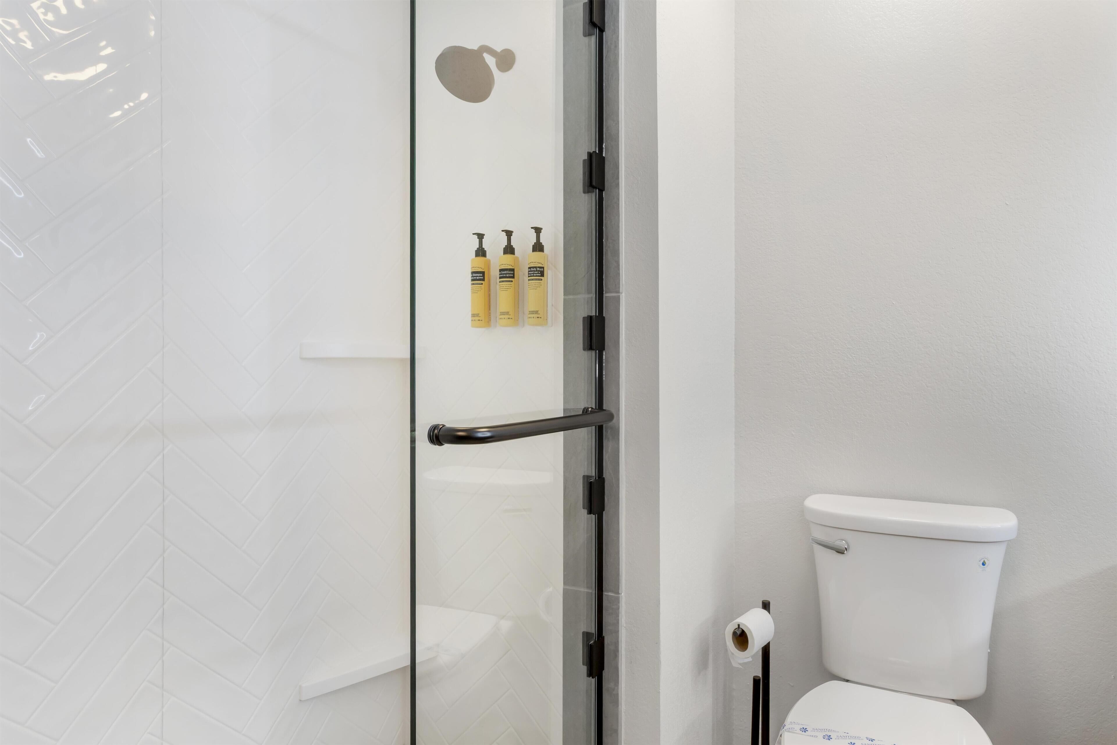 Un baño con cabina de ducha de vidrio, inodoro blanco y tres botellas amarillas en la pared.