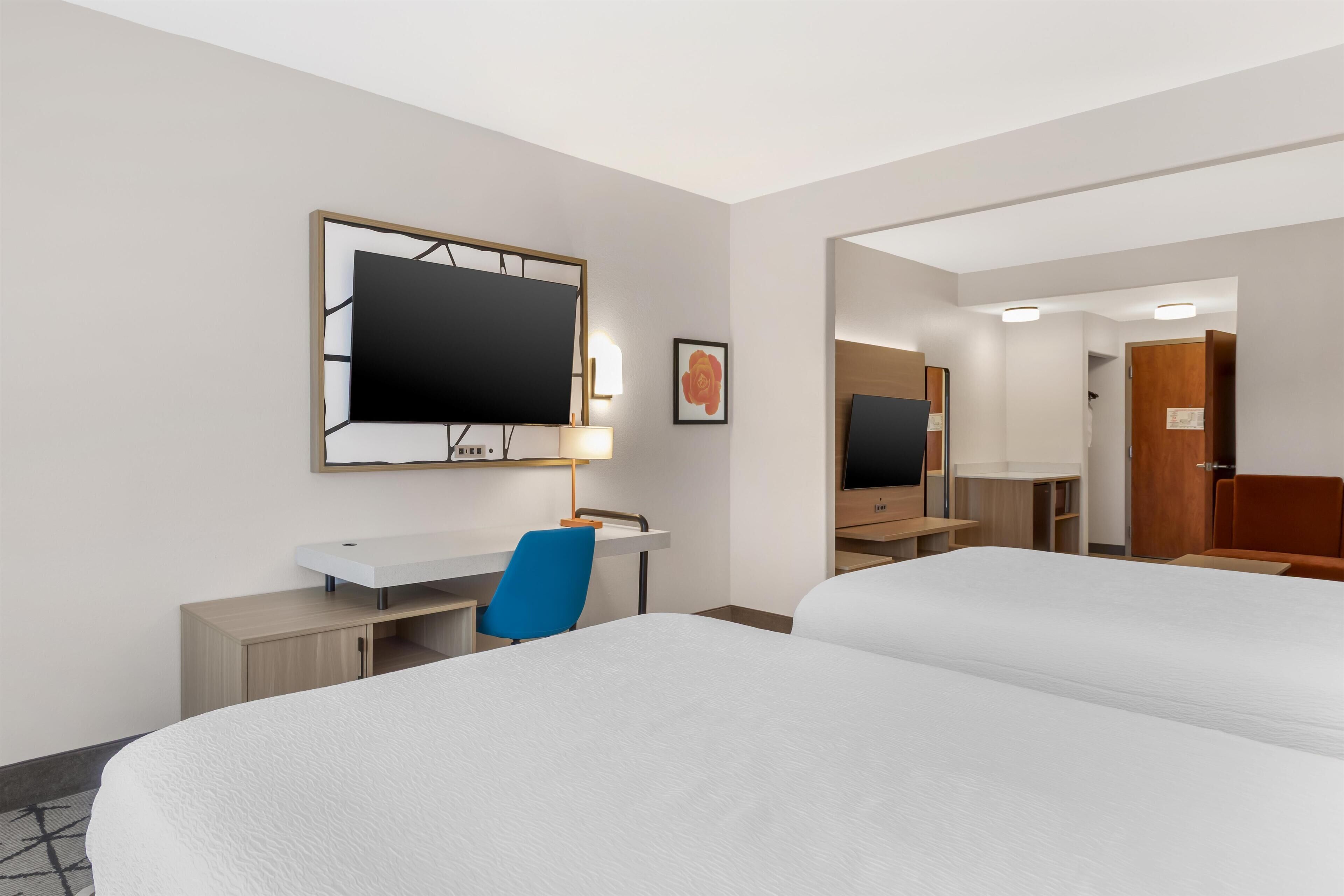 A hotel room with two beds, a desk, a chair, a TV, and a mirror.