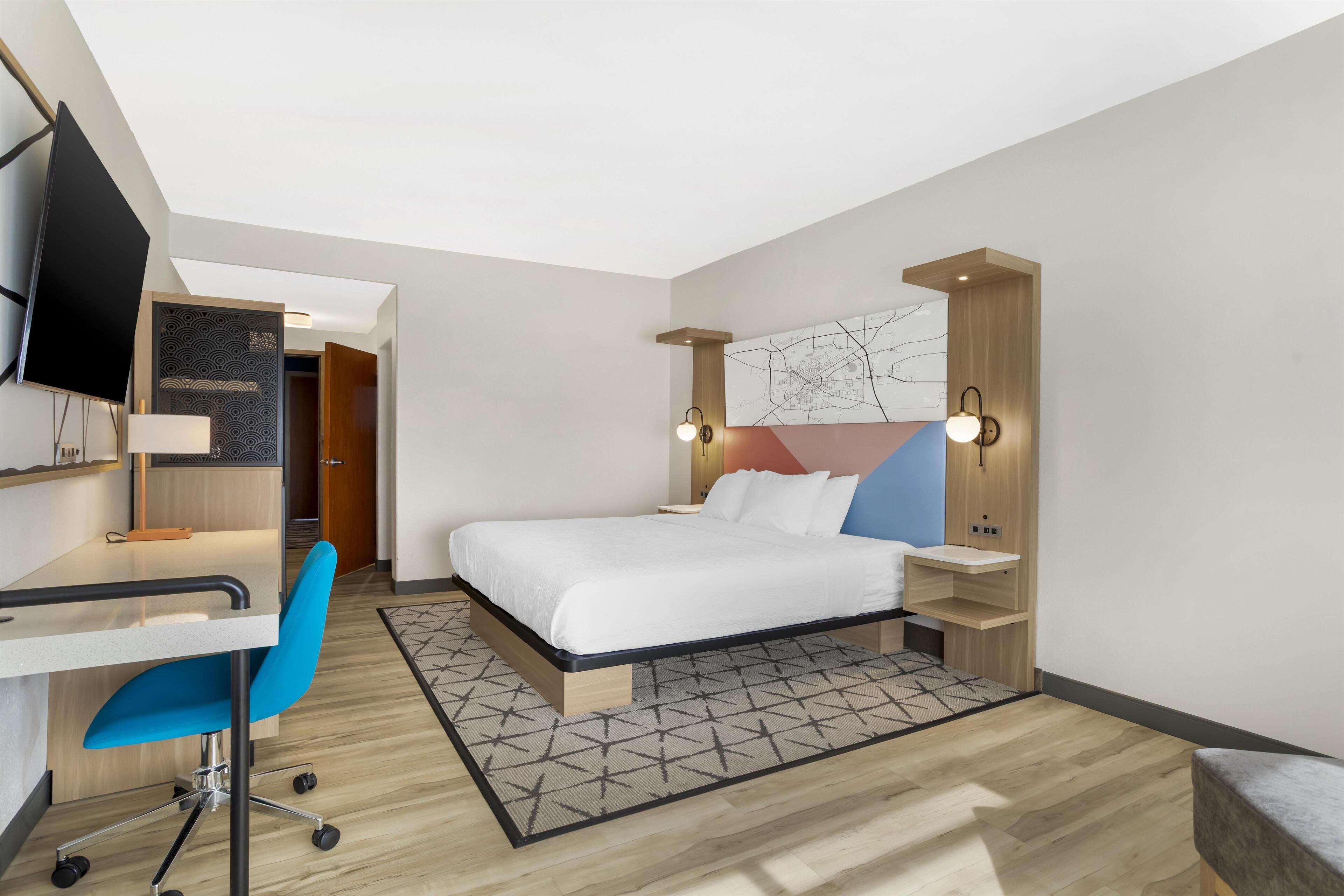 A hotel room with a bed, desk, chair, and a TV.
