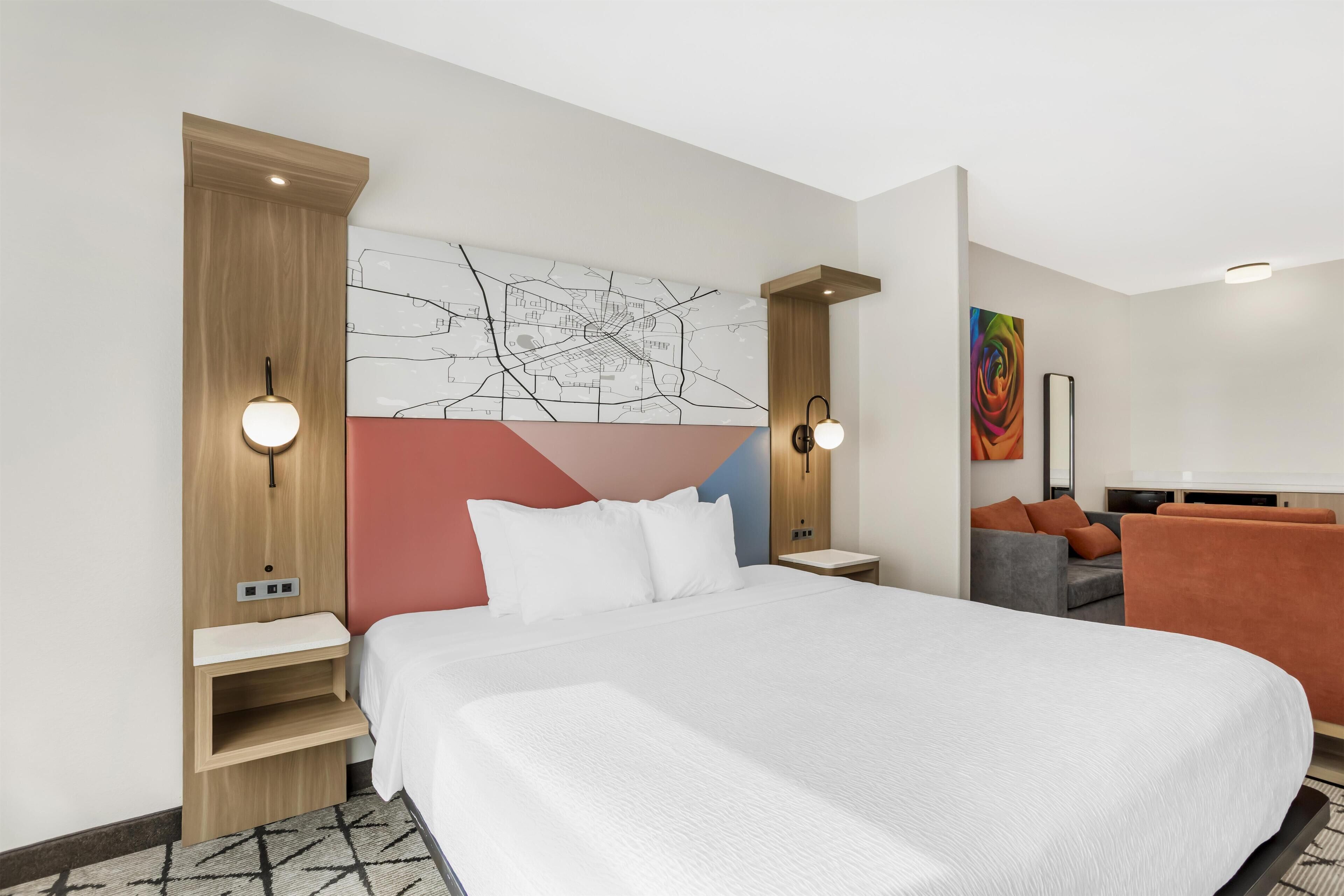 A modern hotel room with a large bed, a desk, a chair, and a sofa.