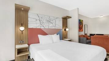A modern hotel room with a large bed, a desk, a chair, and a sofa.