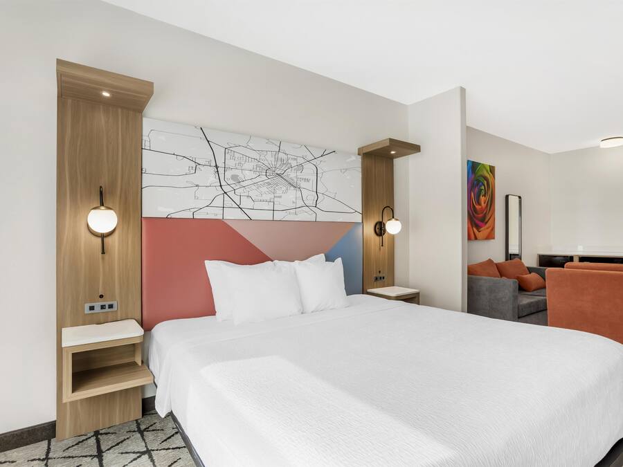 A modern hotel room with a large bed, a desk, a chair, and a sofa.