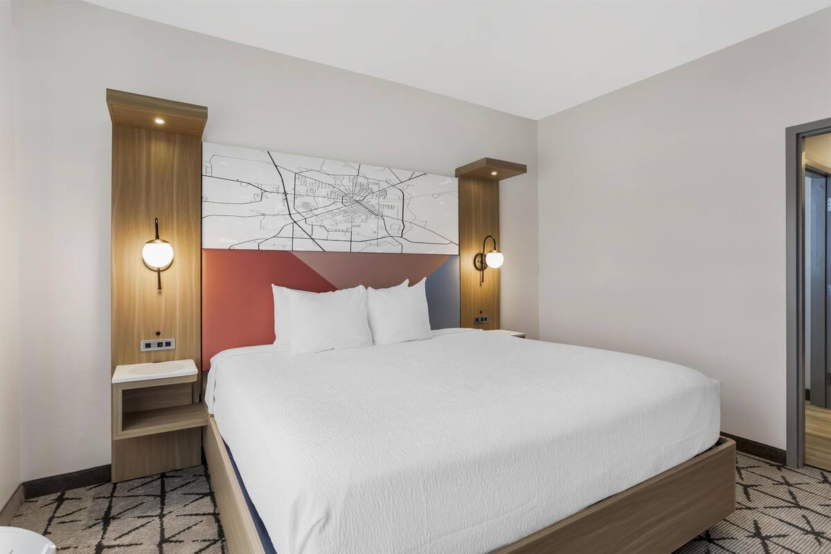 A hotel room with a large bed, wooden headboard, and two wall-mounted reading lamps.