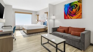 A modern hotel room with a bed, a grey sofa, a desk, and a large abstract painting. - Best Western Plus Rose City Conference Center Inn (Thomasville)
