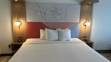 Una habitación de hotel con una cama grande, dos mesitas de noche, un mapa colgado en la pared y dos apliques.