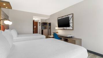 A hotel room with two beds, a desk, a TV, and a kitchenette.