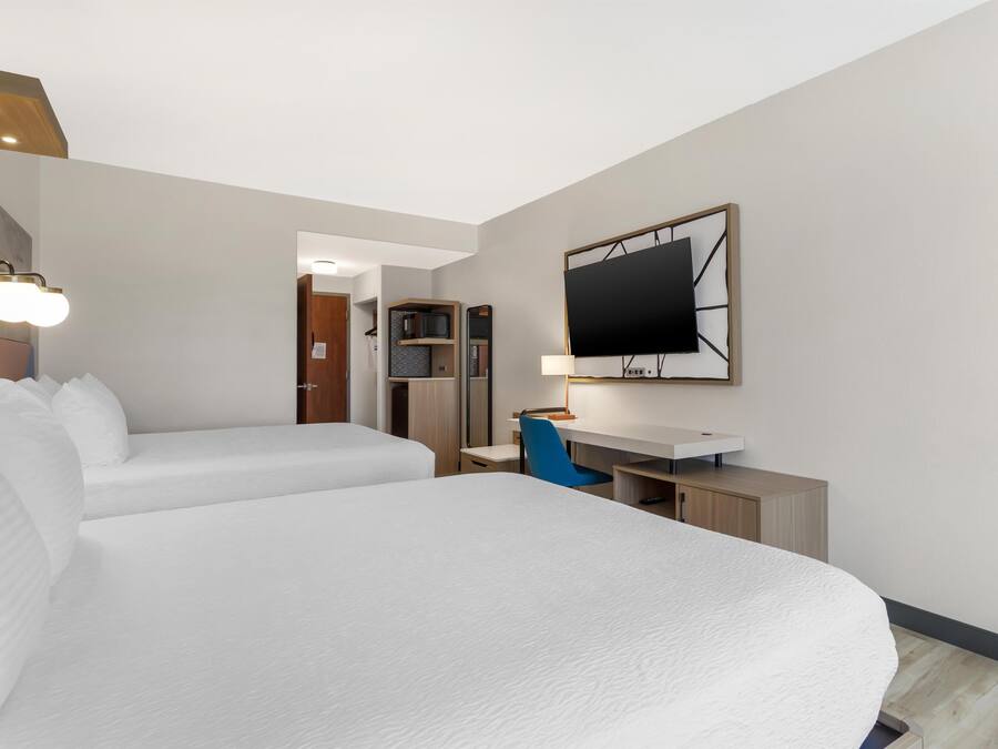 A hotel room with two beds, a desk, a TV, and a kitchenette.