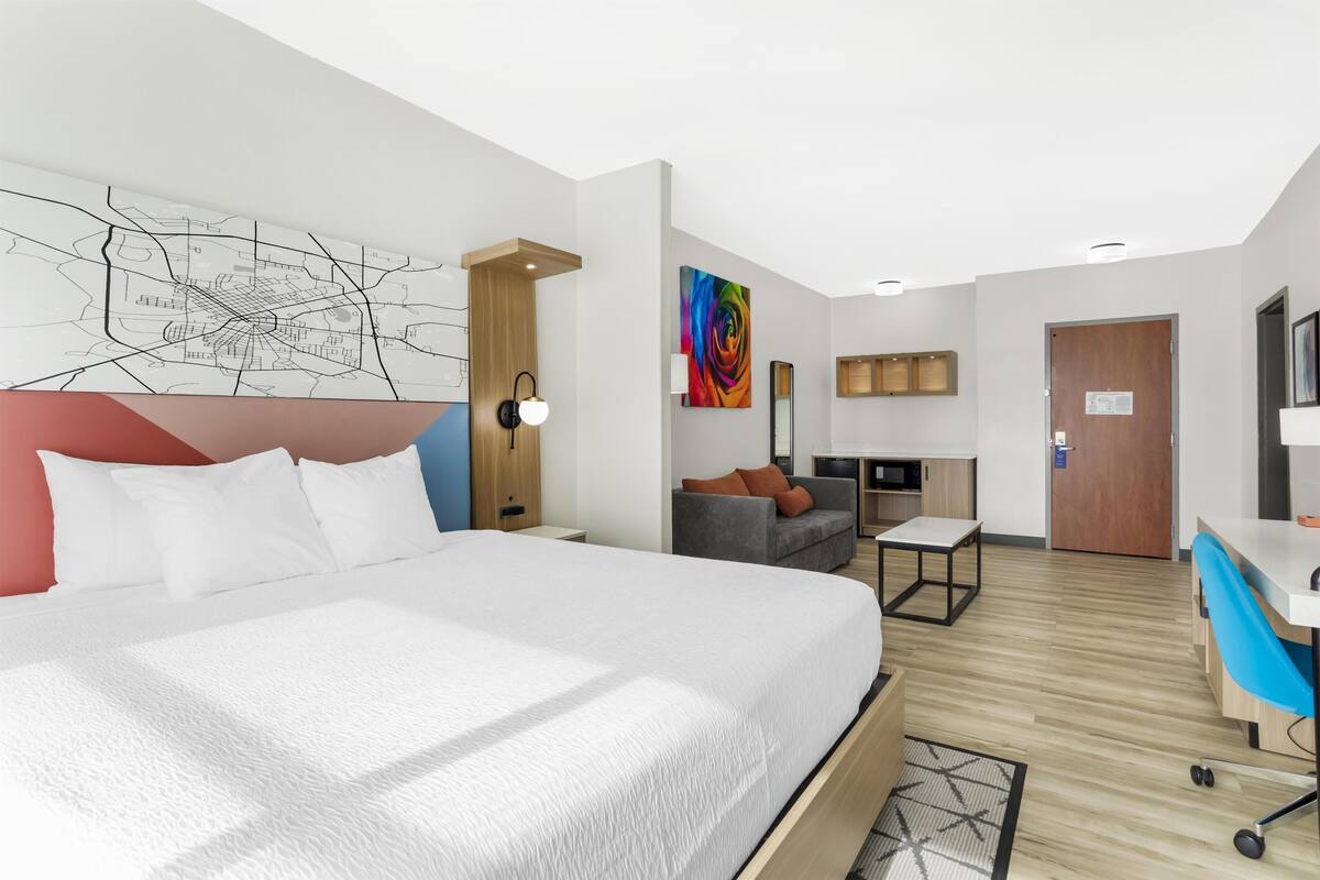 A modern hotel room with a large bed, a desk, a sofa, and a map on the wall.