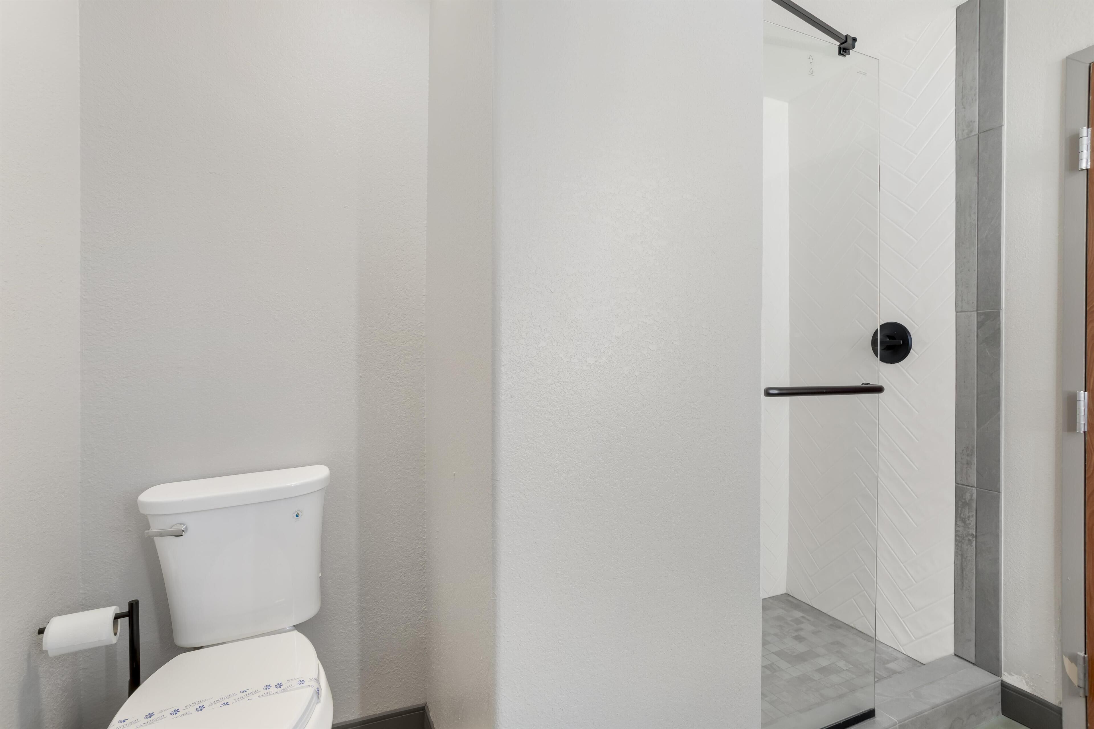 A bathroom with a toilet, a shower area, and a door with a handle.