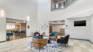 A spacious lobby with a high ceiling, a central seating area with sofas and chairs, a flat-screen TV mounted on the wall, and a staircase leading to an upper level. - Best Western Plus Rose City Conference Center Inn (Thomasville)