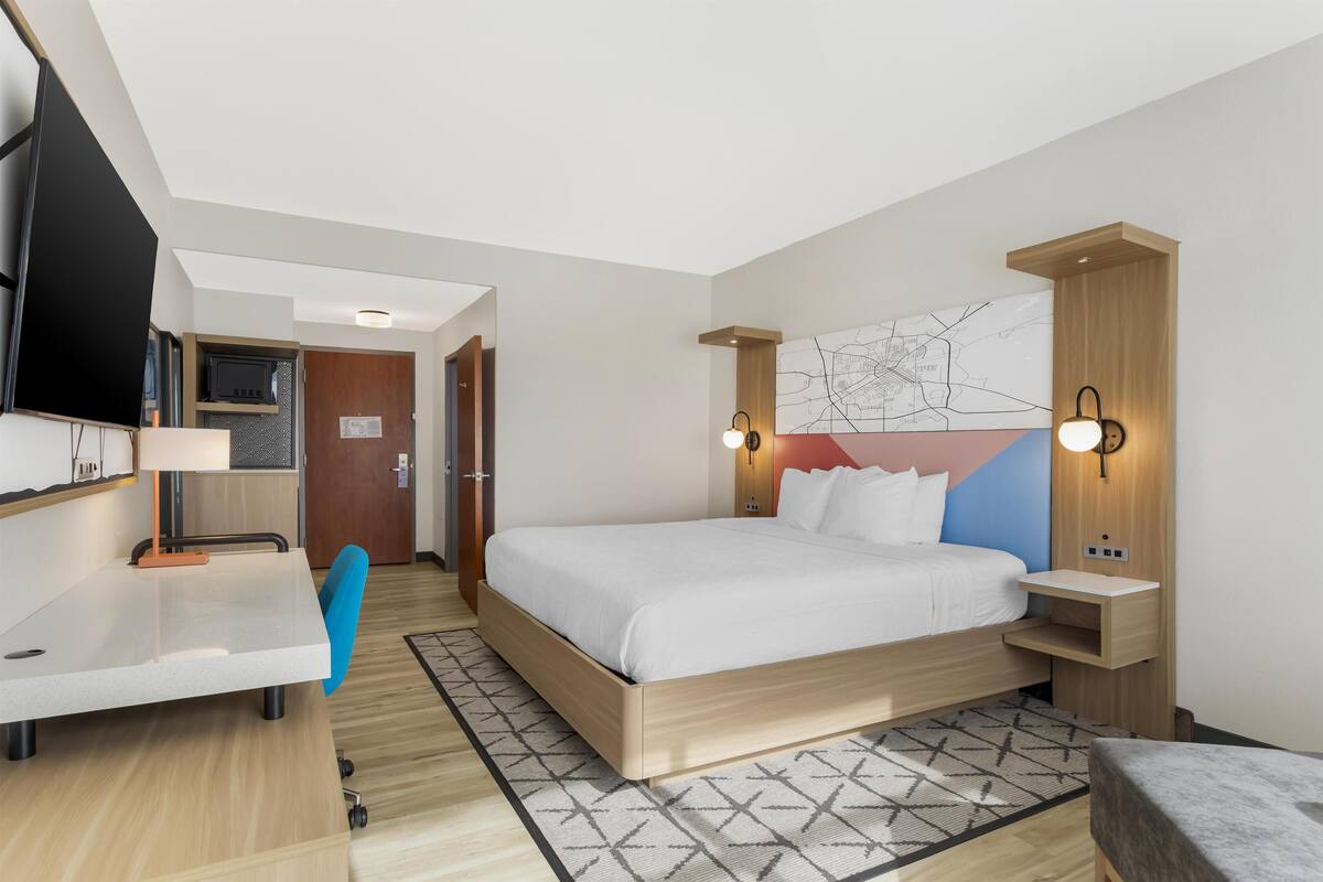 A modern hotel room with a bed, desk, and TV.