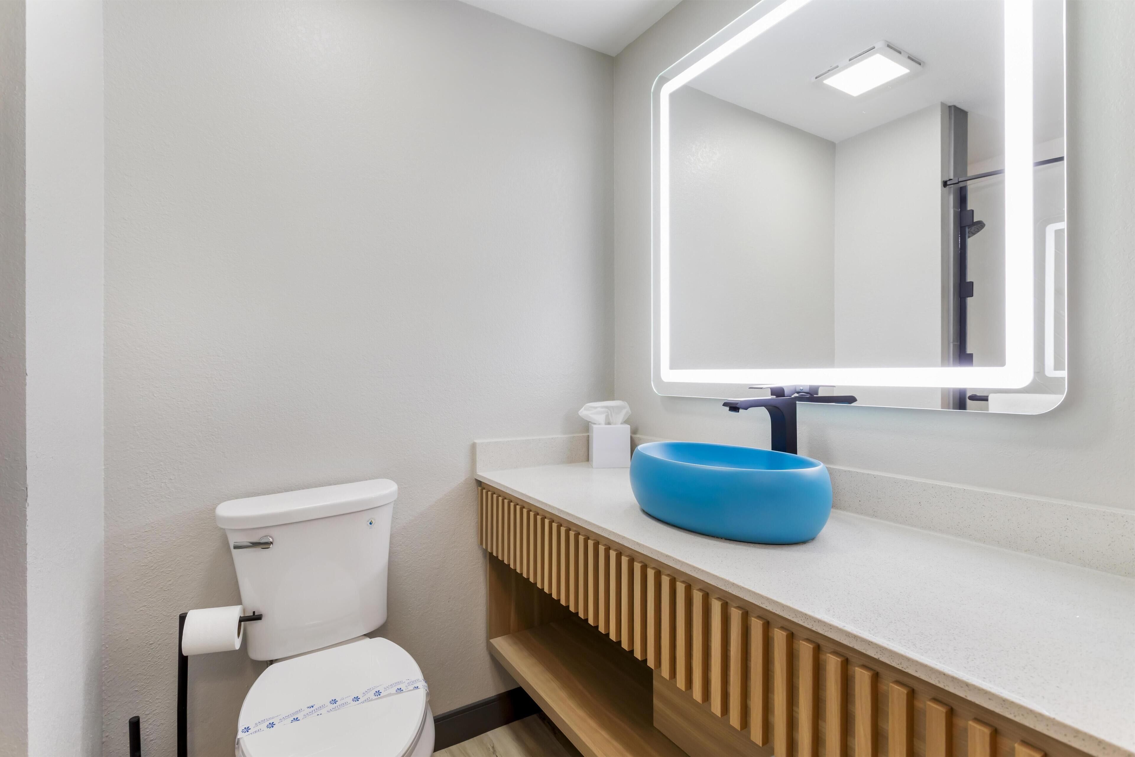 A modern bathroom with a white toilet, a blue sink, and a mirror with integrated lighting.