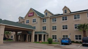 Red Roof Inn & Suites -hotellin rakennus, jossa on katettu sisäänkäynti, useita ikkunoita ja pysäköintialue, jolla on sininen, liikuntarajoitteisille varattu pysäköintipaikka.