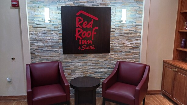 Red Roof Inn -hotellin kyltti, jonka taustalla on kiviseinä, kaksi punaista nahkaista nojatuolia ja pieni pyöreä pöytä aulassa.