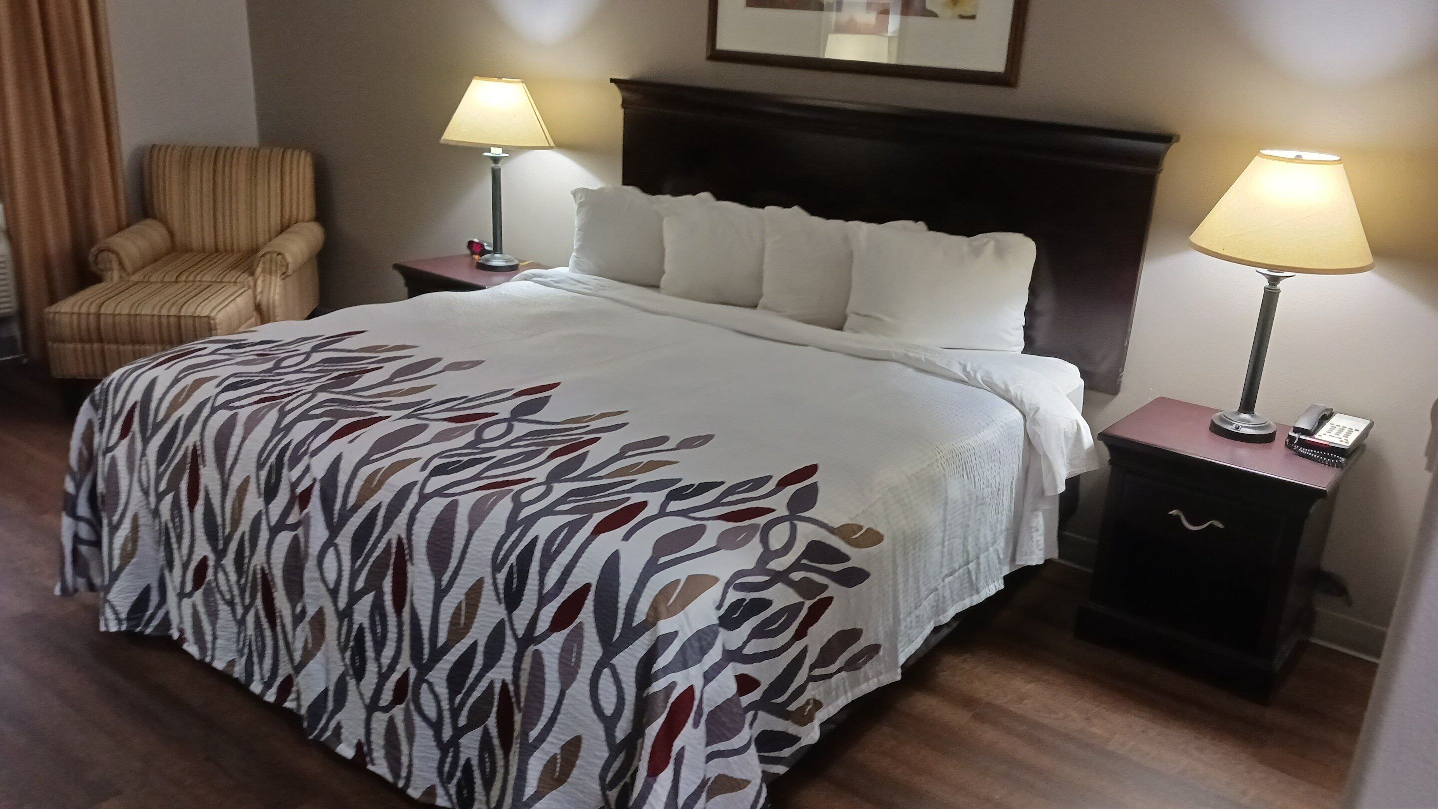 A hotel room with a large bed, two bedside tables with lamps, a chair, and a framed picture on the wall.