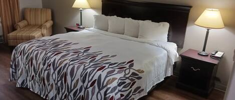 A hotel room with a large bed, two bedside tables with lamps, a chair, and a framed picture on the wall.