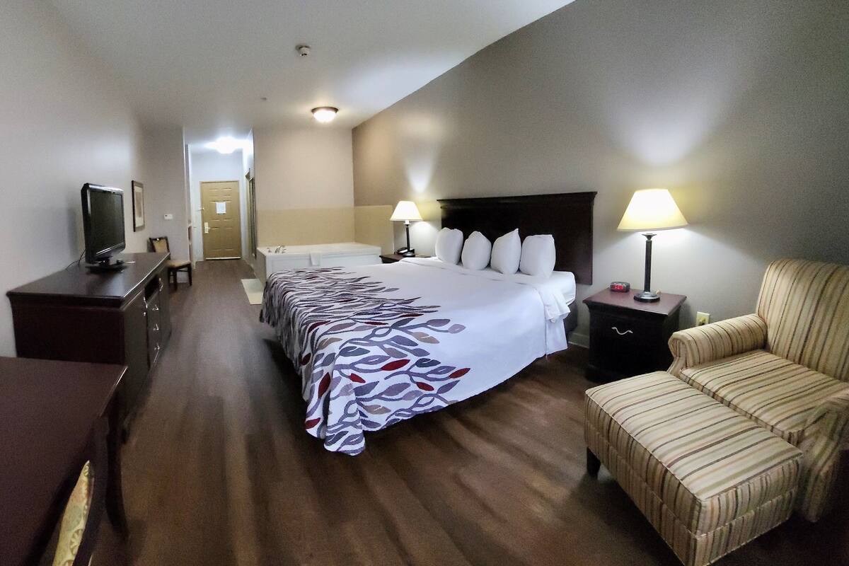 A hotel room with a bed, a chair, a TV, and a desk.