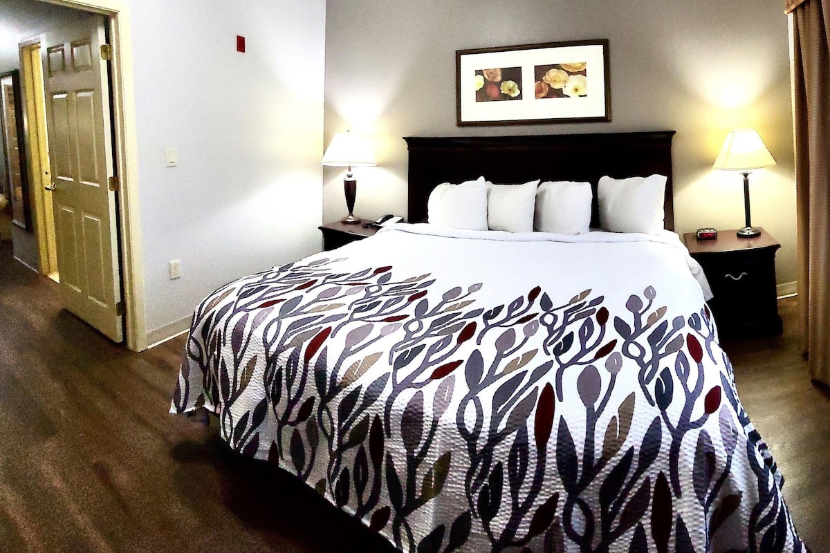 A hotel room with a large bed, two bedside tables with lamps, a framed picture on the wall, and a door to the left.