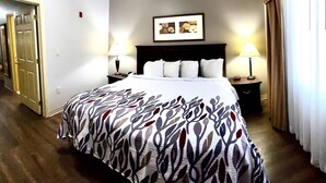 A hotel room with a large bed, two bedside tables with lamps, a framed picture on the wall, and a door to the left. - Red Roof Inn & Suites Midland (Midland)