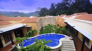 A rooftop swimming pool surrounded by lush greenery and terraced buildings with red-tiled roofs. - Hotel Camino Real Antigua (Antigua Guatemala)