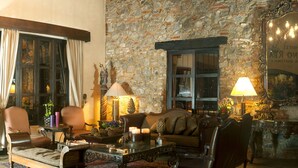 Uma sala de estar aconchegante com parede de pedra, lareira e área de estar confortável com sofá e poltronas.