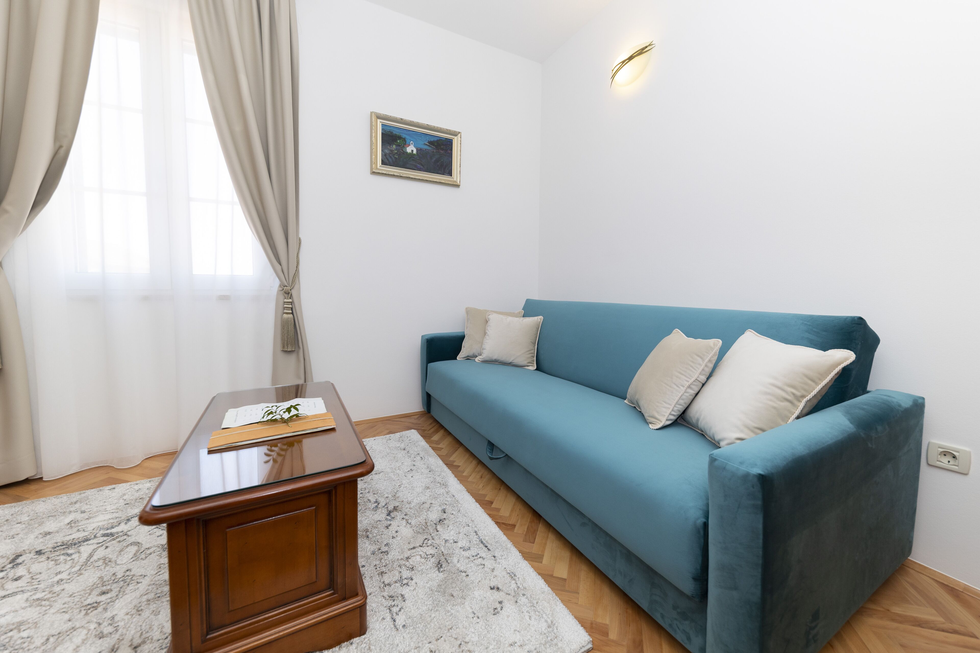 A room with a blue sofa, a wooden side table, a white rug, and a framed picture on the wall.