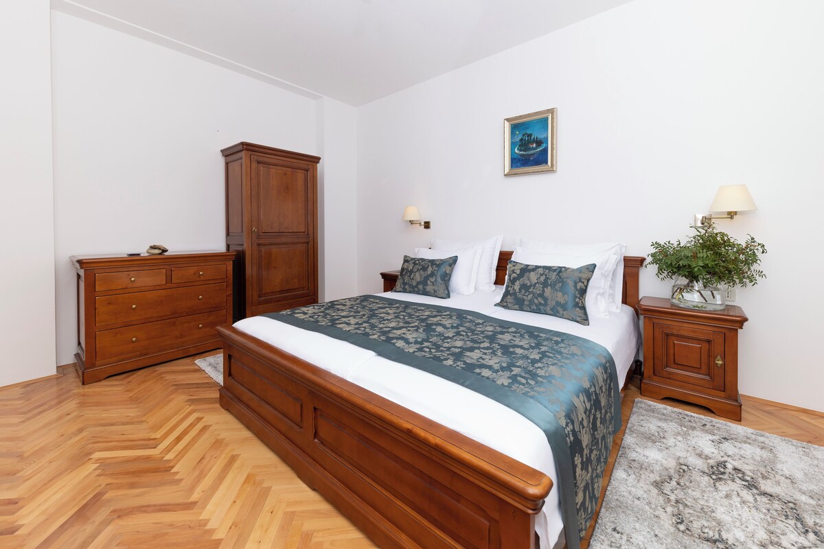 Un dormitorio con cama de madera, cómoda, mesita de noche con lámpara y un cuadro enmarcado en la pared.