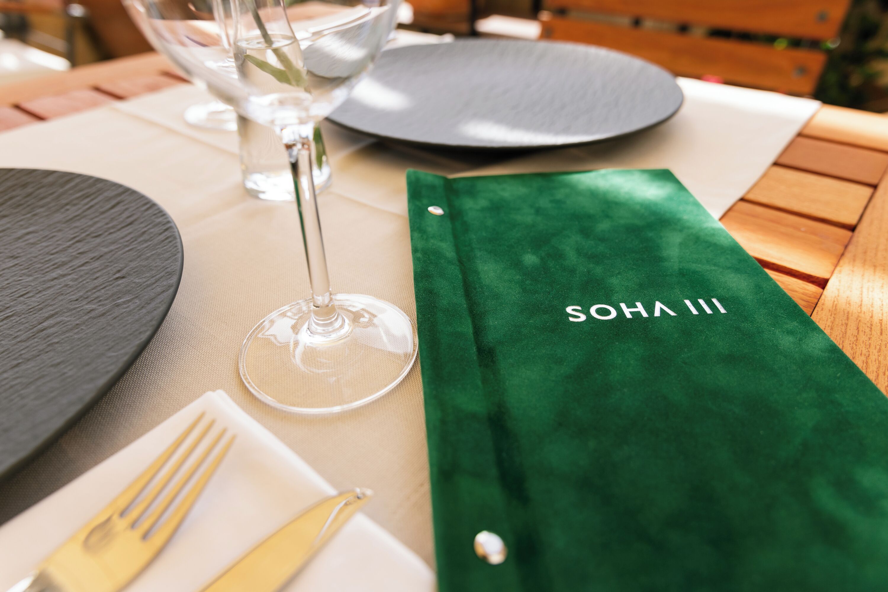 A table set with a green menu, a wine glass, and cutlery.