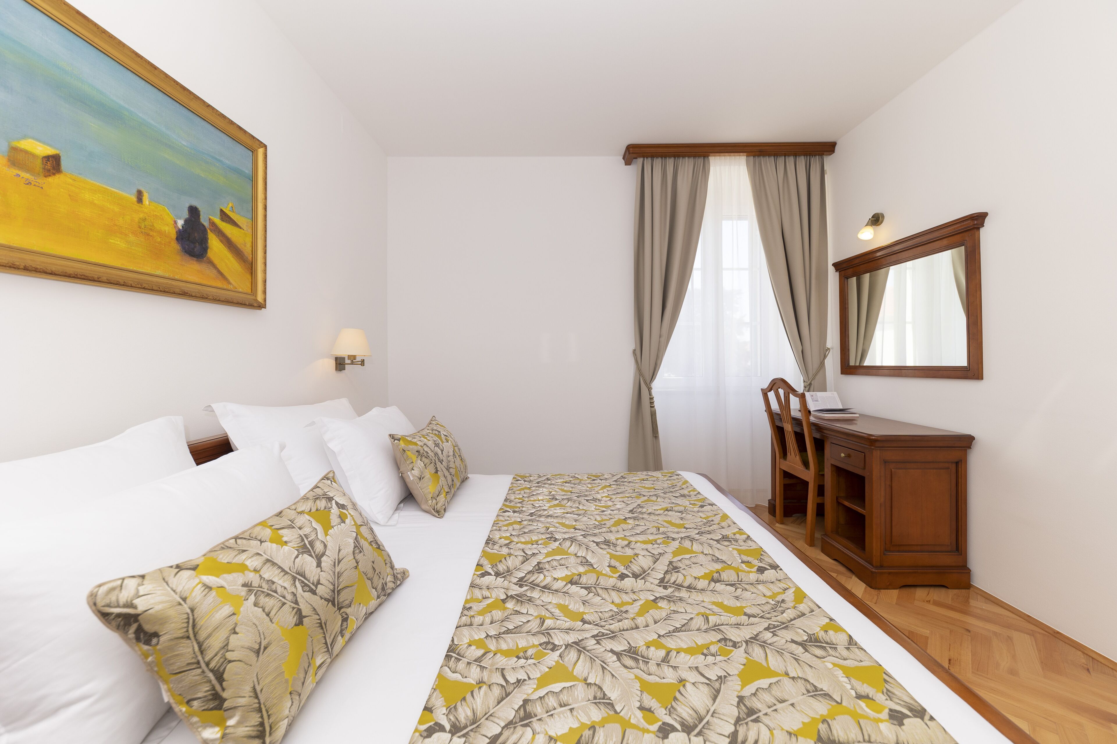 Ein Hotelzimmer mit Bett, Schreibtisch, Stuhl, Spiegel und einem Gemälde an der Wand.