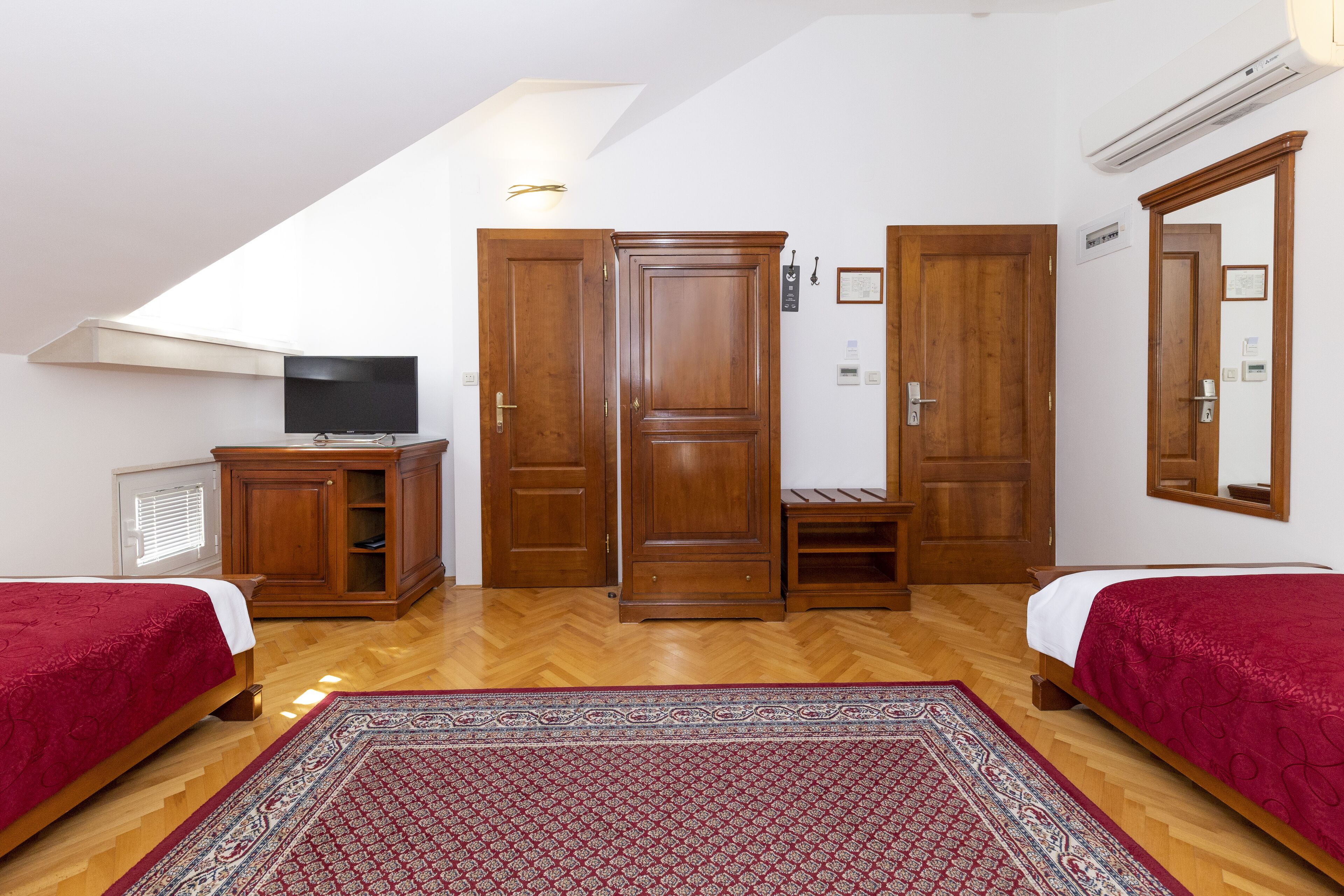 Une chambre avec deux lits, une télévision, une armoire en bois et un grand miroir.