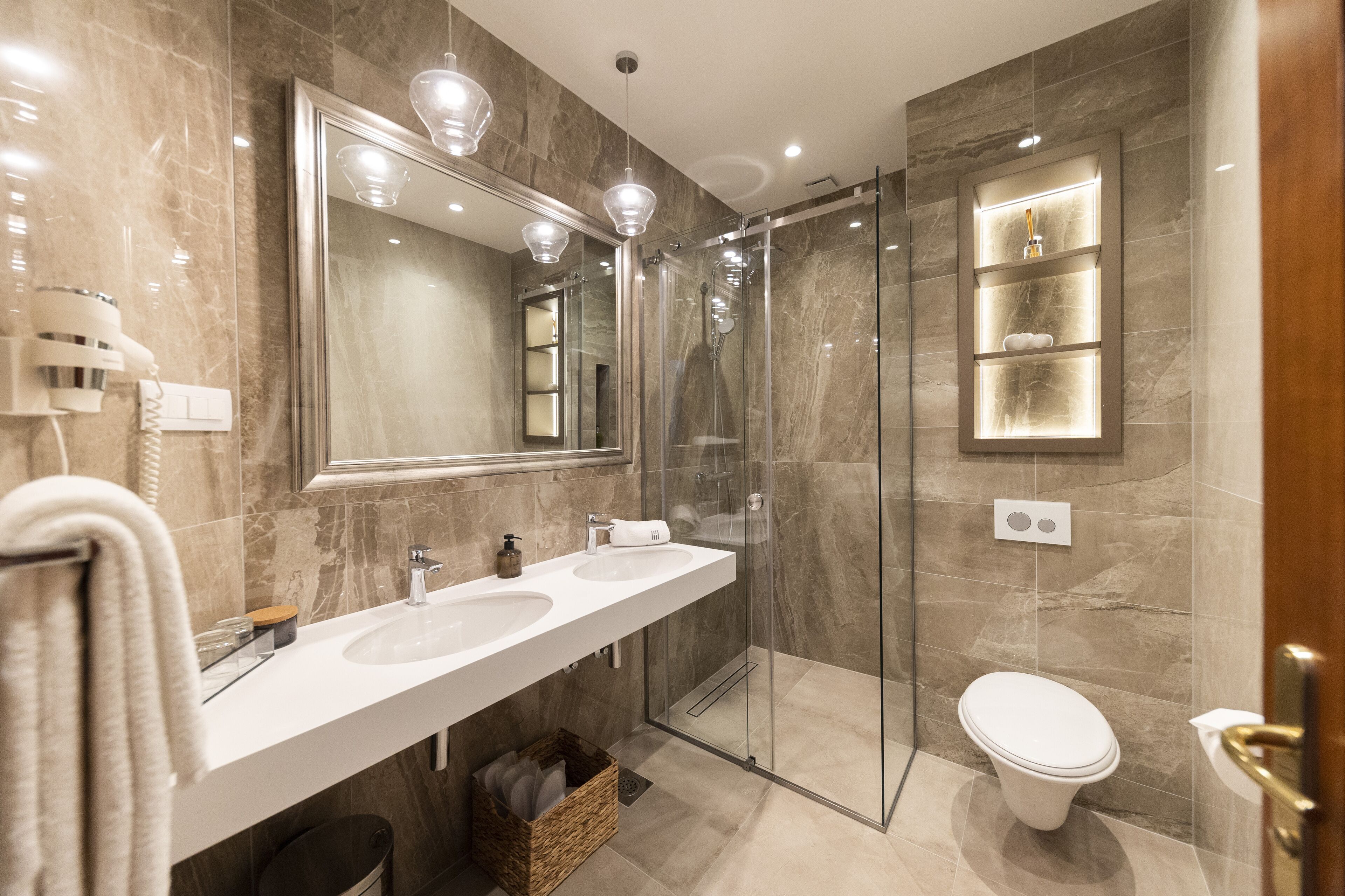 A modern bathroom with two sinks, a glass-enclosed shower, a toilet, and a large mirror.