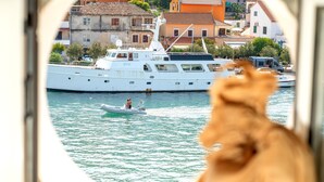 Vista a través de una ventana de un yate grande amarrado en un puerto deportivo, con edificios al fondo.