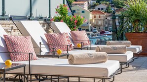 Un área de lounge en la azotea con sillones de sol, almohadones estampados y toallas.