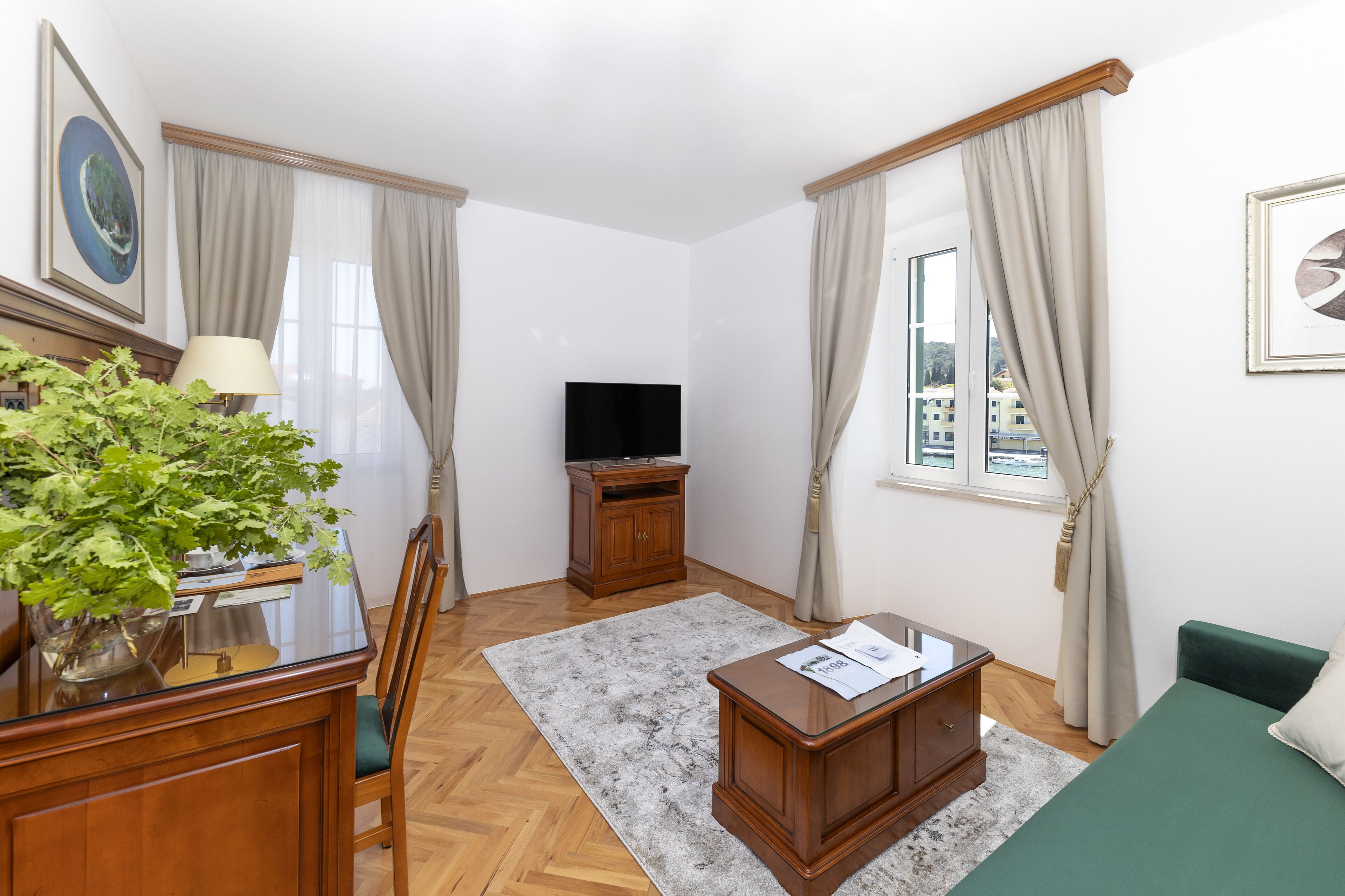 Una habitación de hotel con un escritorio de madera, un televisor sobre un mueble, un sofá verde y una planta en maceta.