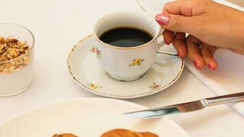 Un desayuno con una taza de café, un vaso de agua con rodajas de limón, un plato con croissants, fresas, arándanos y sandía.