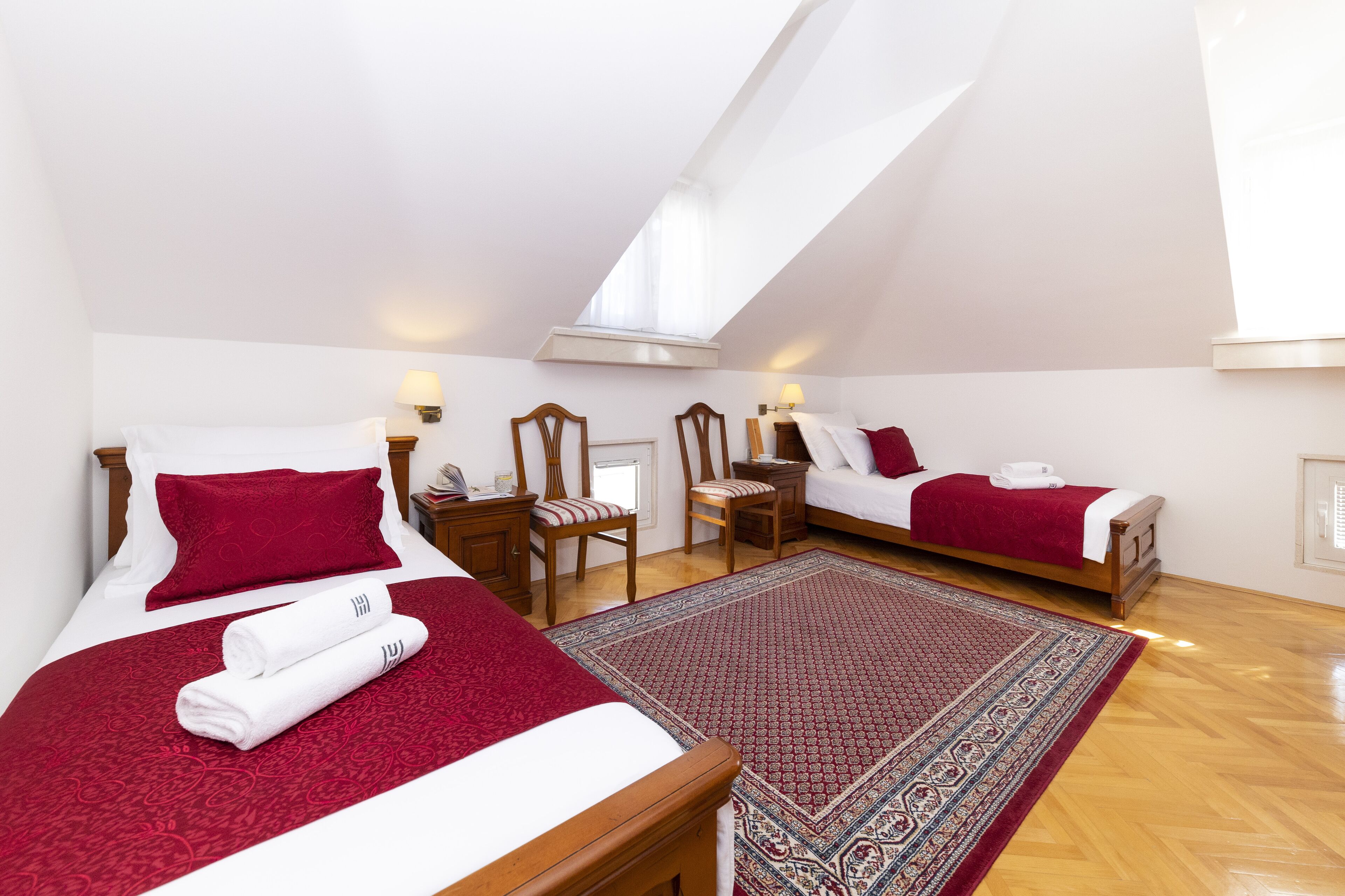 A bedroom with two beds, a large rug, and a skylight.