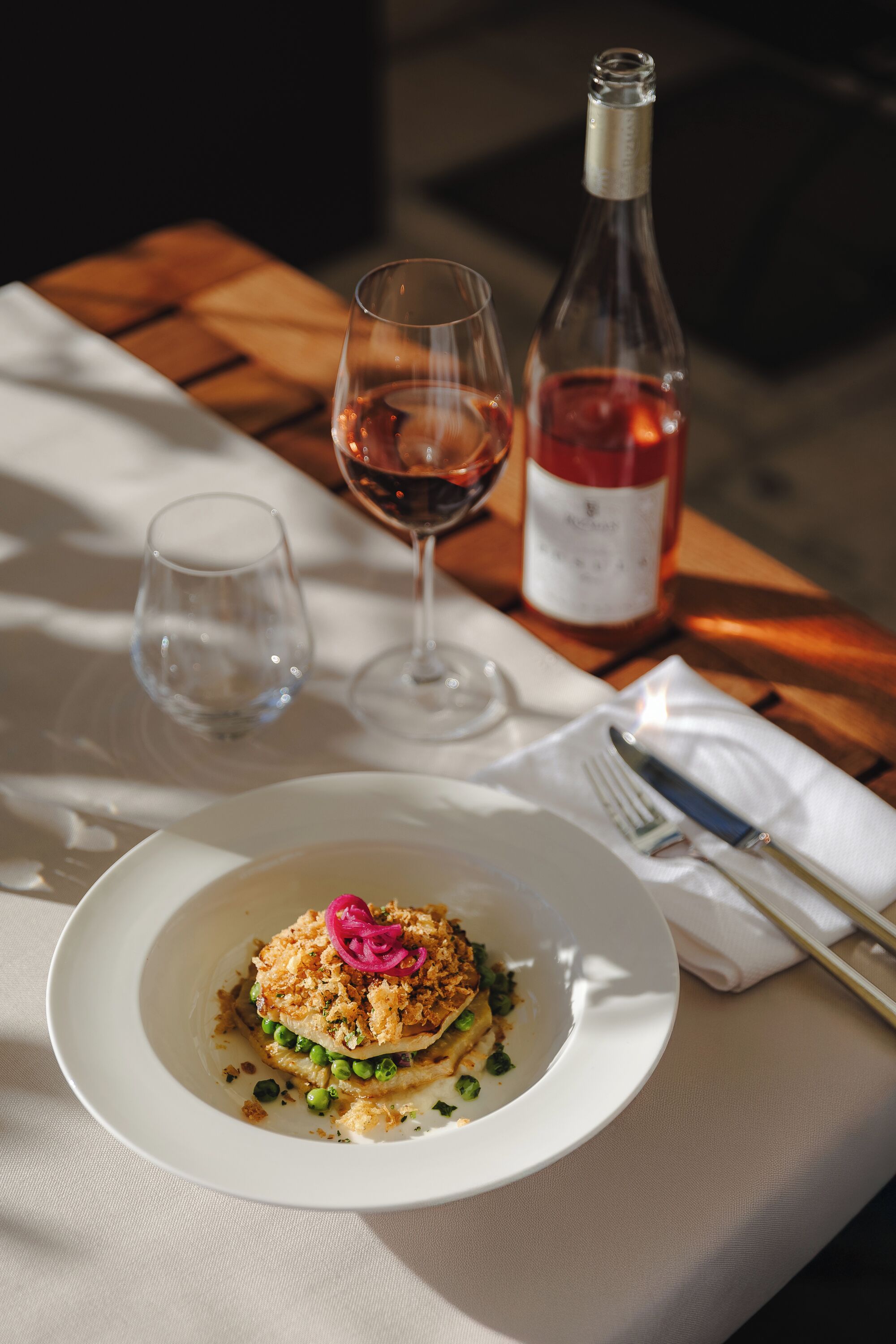 A dining table with a plate of food, a wine bottle, and two glasses.