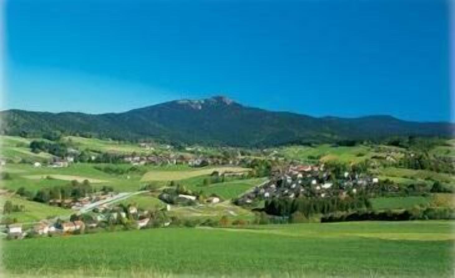 Ländliche Landschaft mit einem Dorf, eingebettet zwischen sanften Hügeln, und einem Berg im Hintergrund.