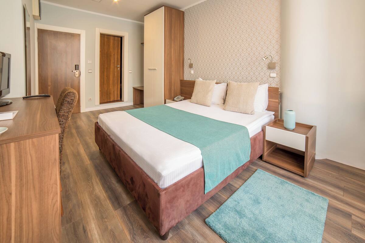 Une chambre d’hôtel avec un grand lit, un bureau avec une chaise, une télévision et une armoire.