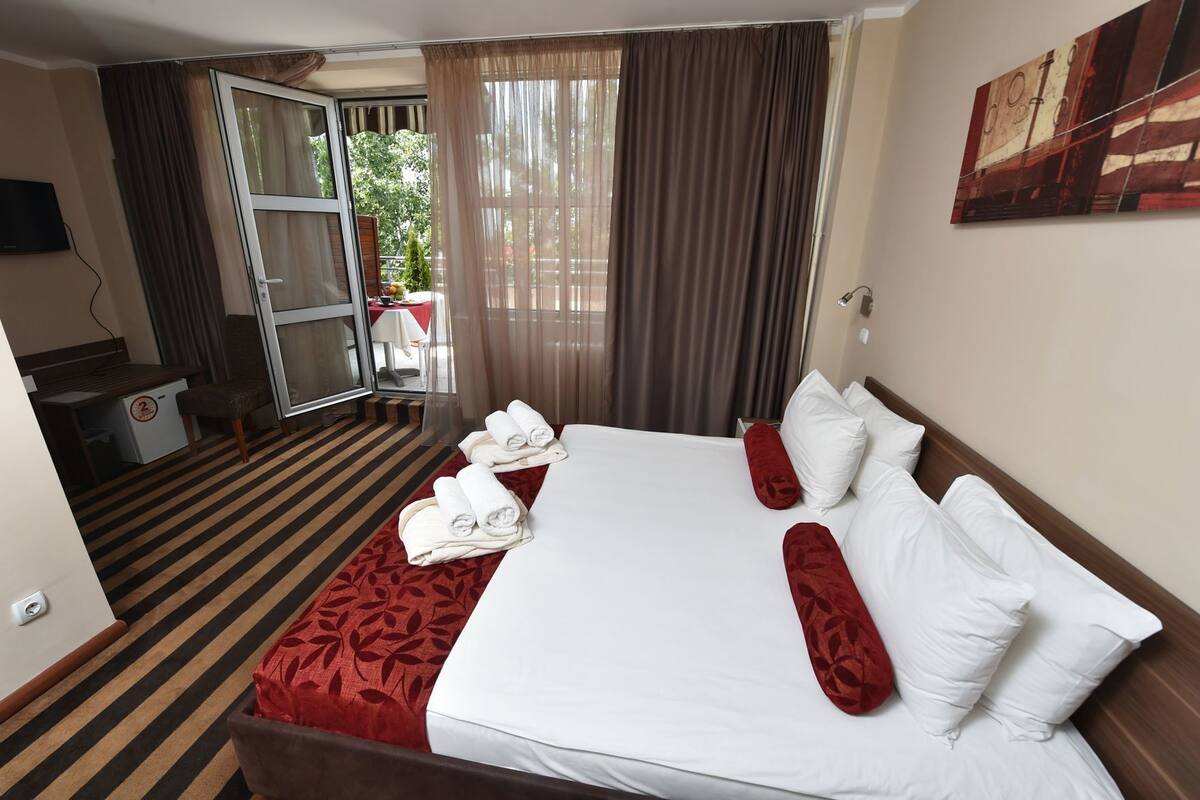 Une chambre d’hôtel avec un lit, un bureau, une chaise, une télévision et une fenêtre avec des rideaux.