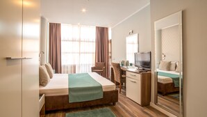 Habitació d'hotel amb llit, escriptori, cadira, televisió i un mirall gran.