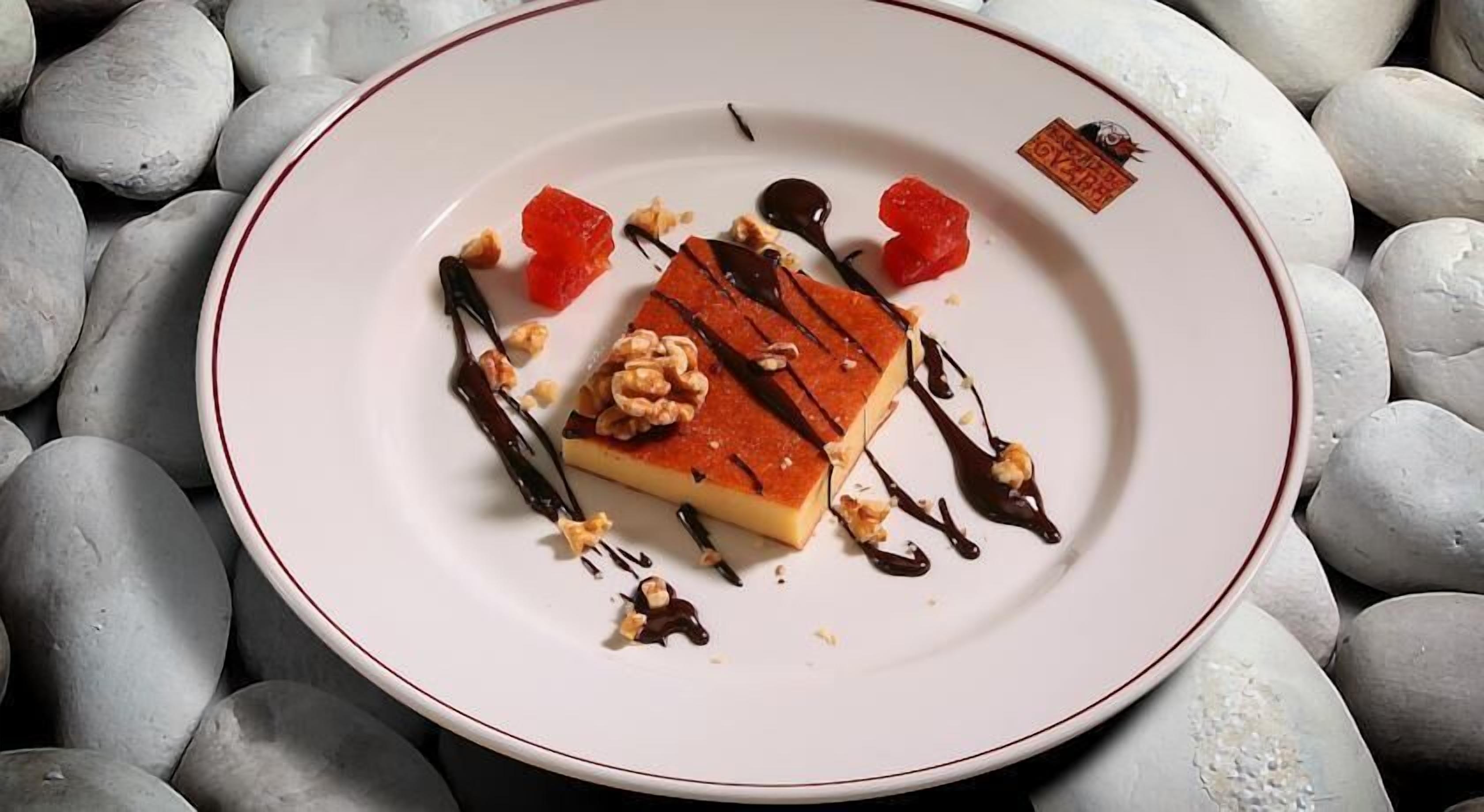 Un dessert présenté dans une assiette à bordure rouge, entouré de quelques noix éparpillées et nappé de chocolat fondu.