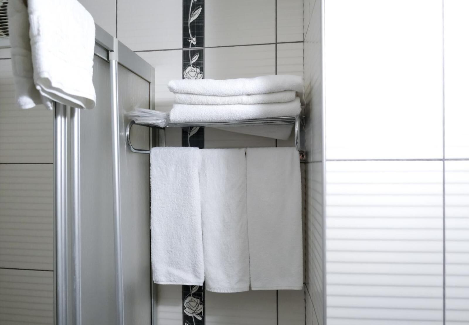 Un baño con azulejos blancos, un perchero con toallas dobladas y una zona de ducha.