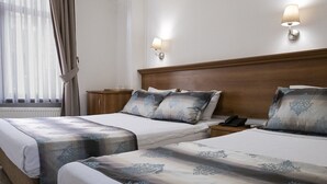 A hotel room with two beds, a wooden headboard, bedside lamps, a nightstand, and a window with curtains. - Kıspet Konak Hotel (Çanakkale)
