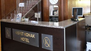 A reception desk at KISPET KONAK HOTEL with a wooden interior, a glass partition, a clock, and a computer monitor. - Kıspet Konak Hotel (Çanakkale)