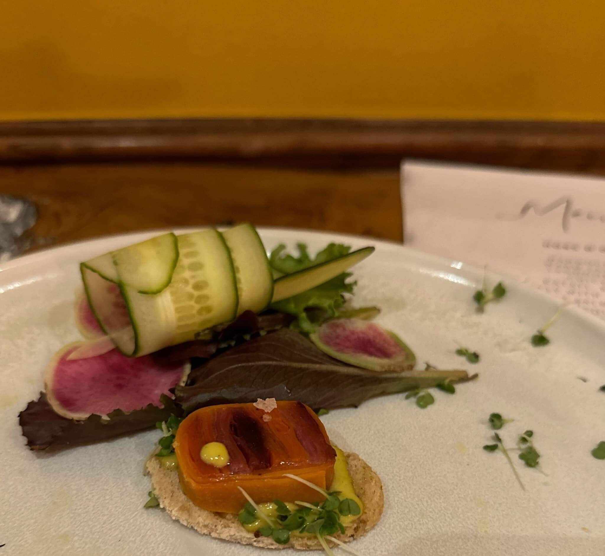 A plate with various food items including a slice of meat, a piece of cheese, and some vegetables.