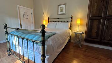 A neatly made bed with a wooden headboard, a bedside table with a lamp, and a wooden wardrobe in a well-lit room with wooden flooring.