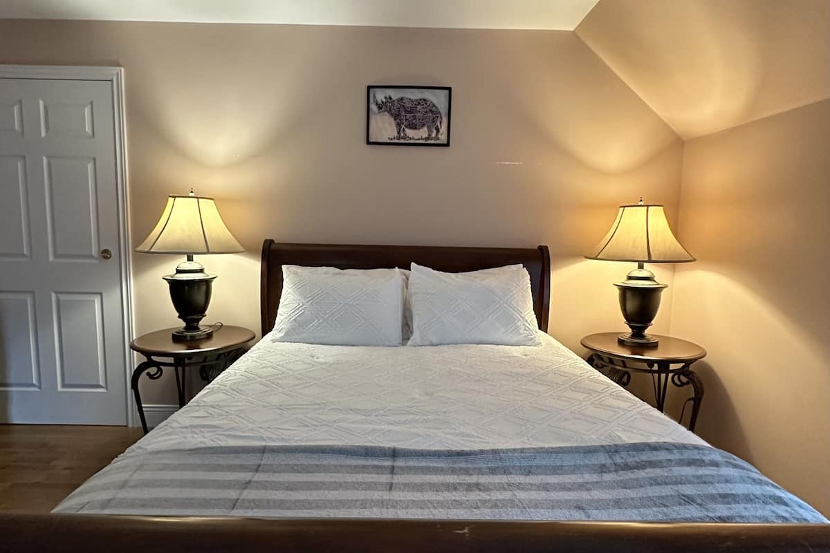 Una cama bien hecha con una colcha a rayas, dos lámparas de noche y un cuadro en la pared.